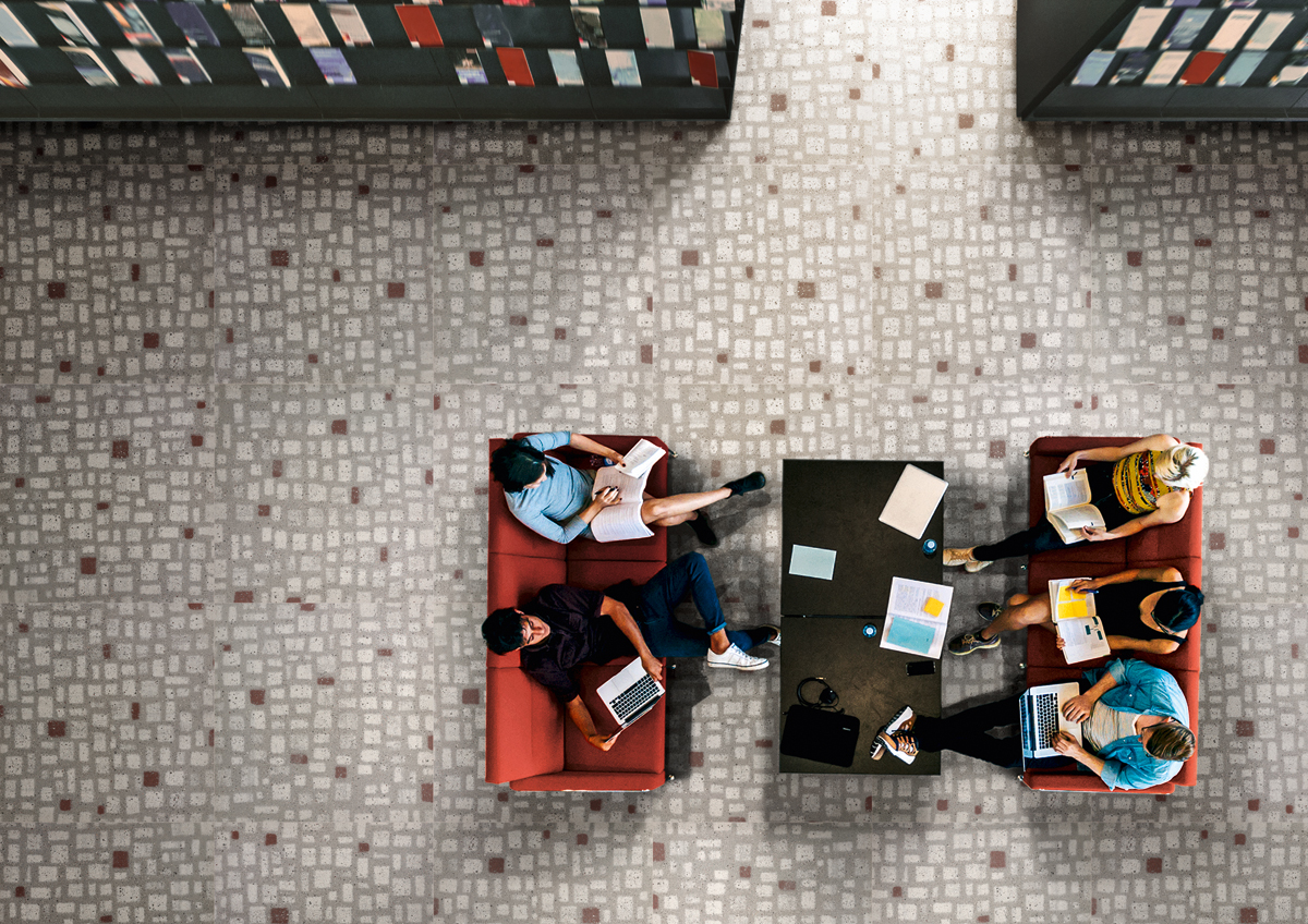 Top view of university students sitting in a library with books and laptop. Young people studying together at college library.
